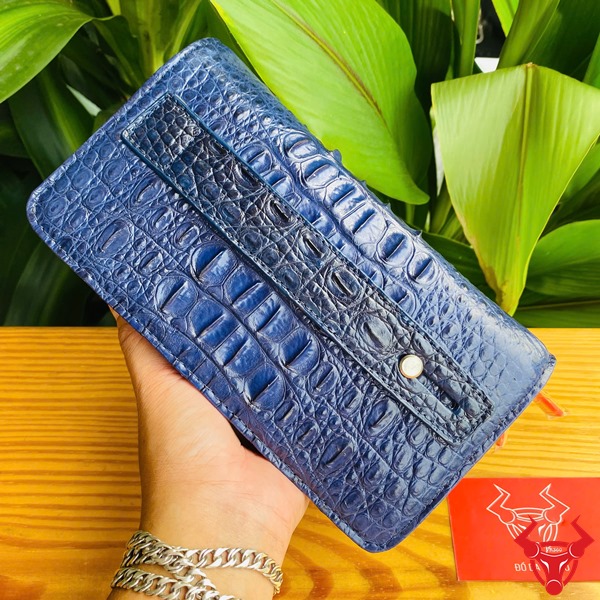 Cao Cấp Đẳng Cấp: Ví Da Cá Sấu Gù BIA4 Xanh Navy Thời Trang Sang Trọng Tiện Dụng Ảnh ví da cá sấu xanh navy cao cấp, nền lá xanh, kèm thẻ thương hiệu đỏ.