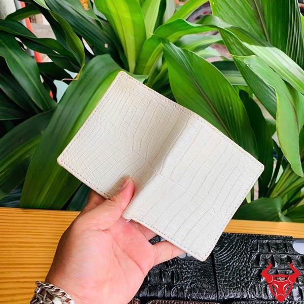 Ví Mini VSAA8 Da Bụng Cá Sấu Trắng – Sản Phẩm Thời Trang Cao Cấp Đẳng Cấp Chiếc ví mini trắng mộc da bụng cá sấu VSAA8 trên tay, bên cạnh lá cây xanh và điện thoại đen.