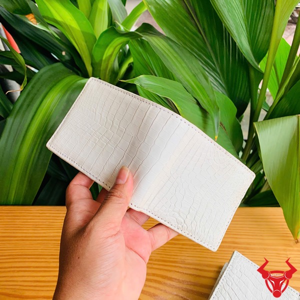 VGA8 Trắng Mộc Da Cá Sấu – Phụ Kiện Thời Trang Cao Cấp Đẳng Cấp Ảnh ví da cá sấu trắng mộc VGA8 hai mặt, cầm tay với nền thực vật xanh.