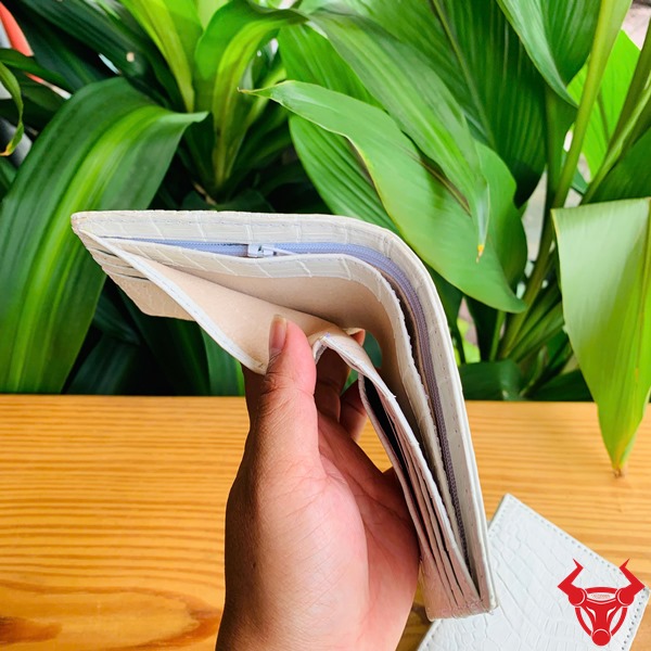 Da Cá Sấu VGA8 Trắng Mộc – Ví Thời Trang Cao Cấp Đẳng Cấp Sang Trọng Hình ảnh cầm ví da cá sấu trắng mộc VGA8, nền gỗ và cây xanh xung quanh.