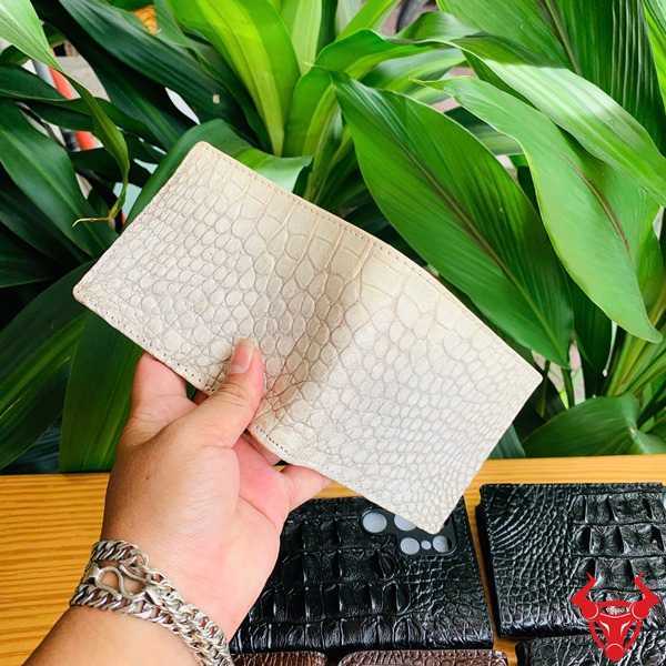 Đẳng Cấp Sang Trọng: Ví Da Bụng Cá Sấu VCA8 Màu Trắng Thời Trang Cao Cấp Ảnh ví nam da bụng cá sấu màu trắng bạch tạng sang trọng, cầm trên tay với nền thực vật xanh và các sản phẩm da khác.
