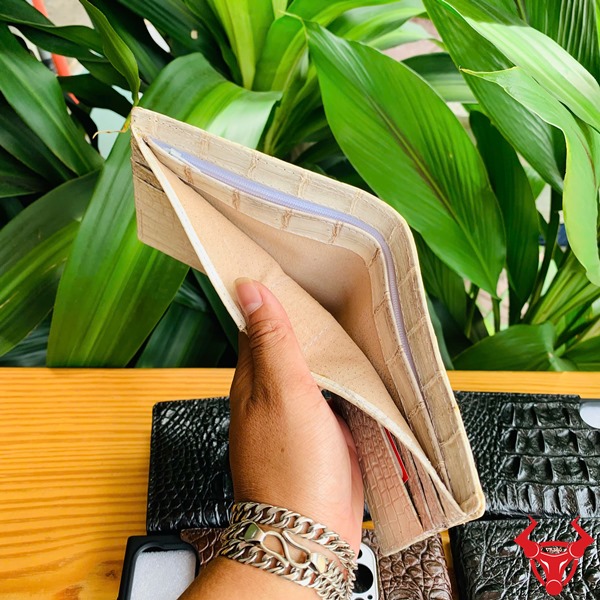 Cao Cấp Đẳng Cấp: Ví Da Cá Sấu VCA8 Bạch Tạng Thời Trang Sang Trọng Ảnh cầm ví nam da cá sấu màu trắng bạch tạng đẳng cấp, với các ví da khác màu và nền xanh thực vật.