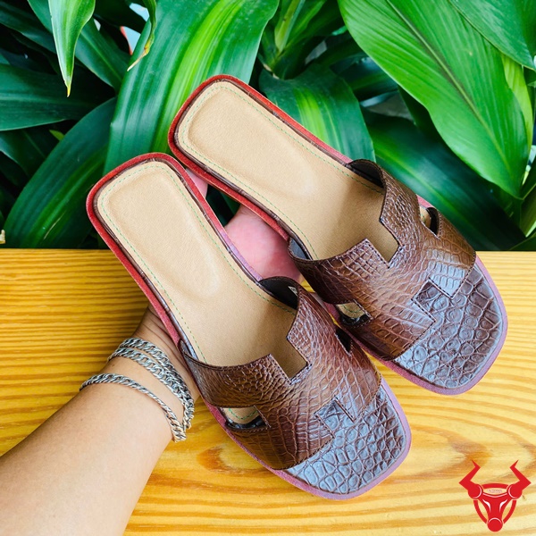 Dép da cá sấu cao cấp thời trang, bền đẹp êm chân hàng ngày. Hình ảnh đôi dép nữ chữ H da cá sấu DJBA9 màu nâu đất với logo thương hiệu.