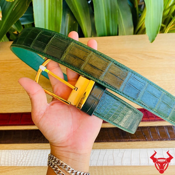 Thắt Lưng Da Cá Sấu Xanh Lá Cao Cấp - Sang Trọng Nam Tính Chiếc thắt lưng da bụng cá sấu xanh lá óng ánh với khóa kim vàng, cầm tay trước nền lá xanh tươi, biểu tượng thời trang cao cấp.